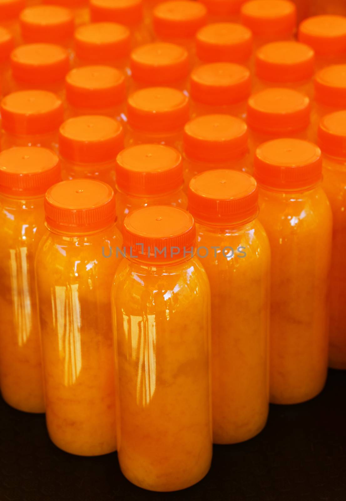 Close up many plastic bottles of fresh orange juice at retail display, high angle view