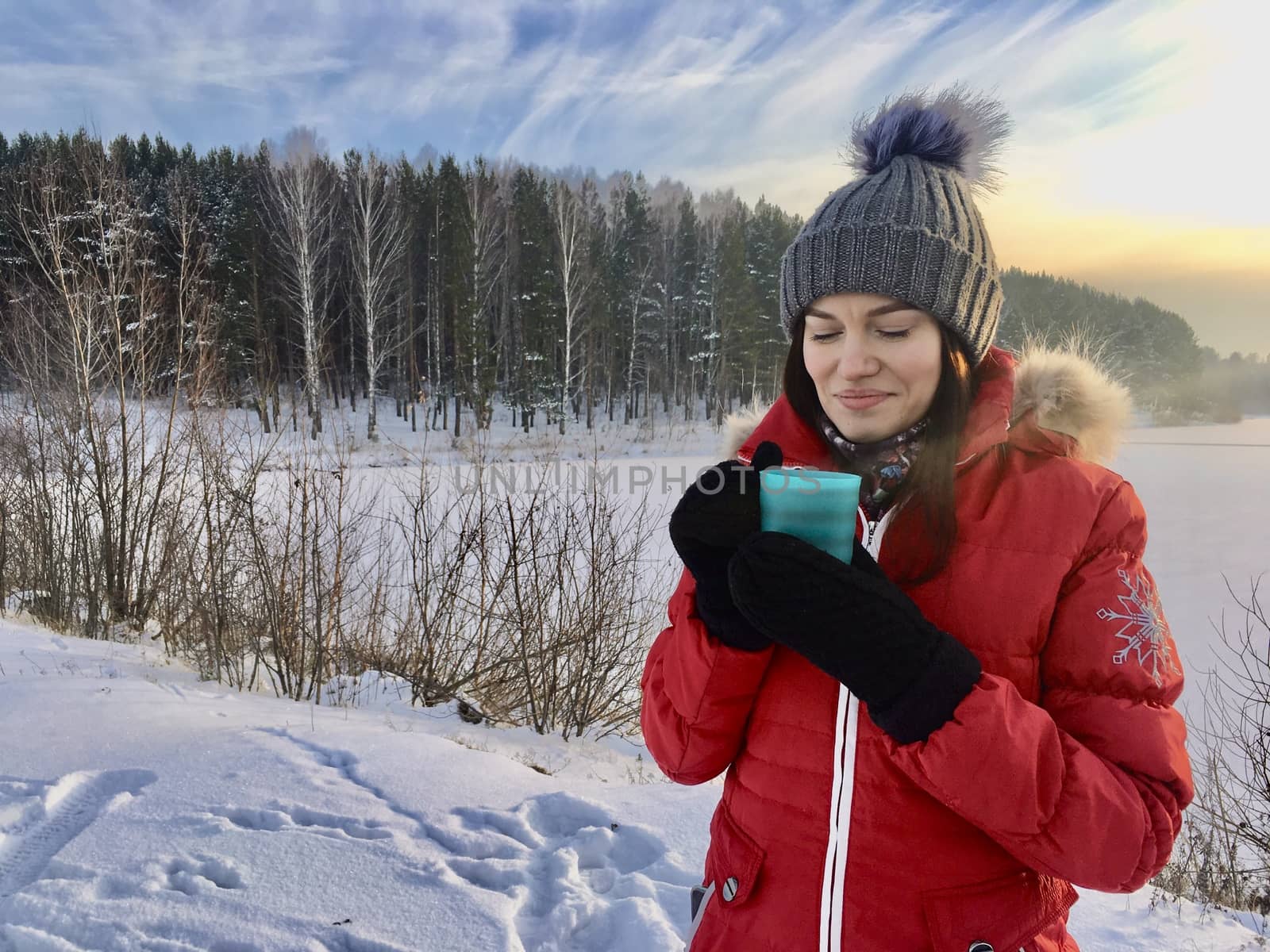 Beautiful girl in a winter jacket with a mug in winter in nature. by AnatoliiFoto