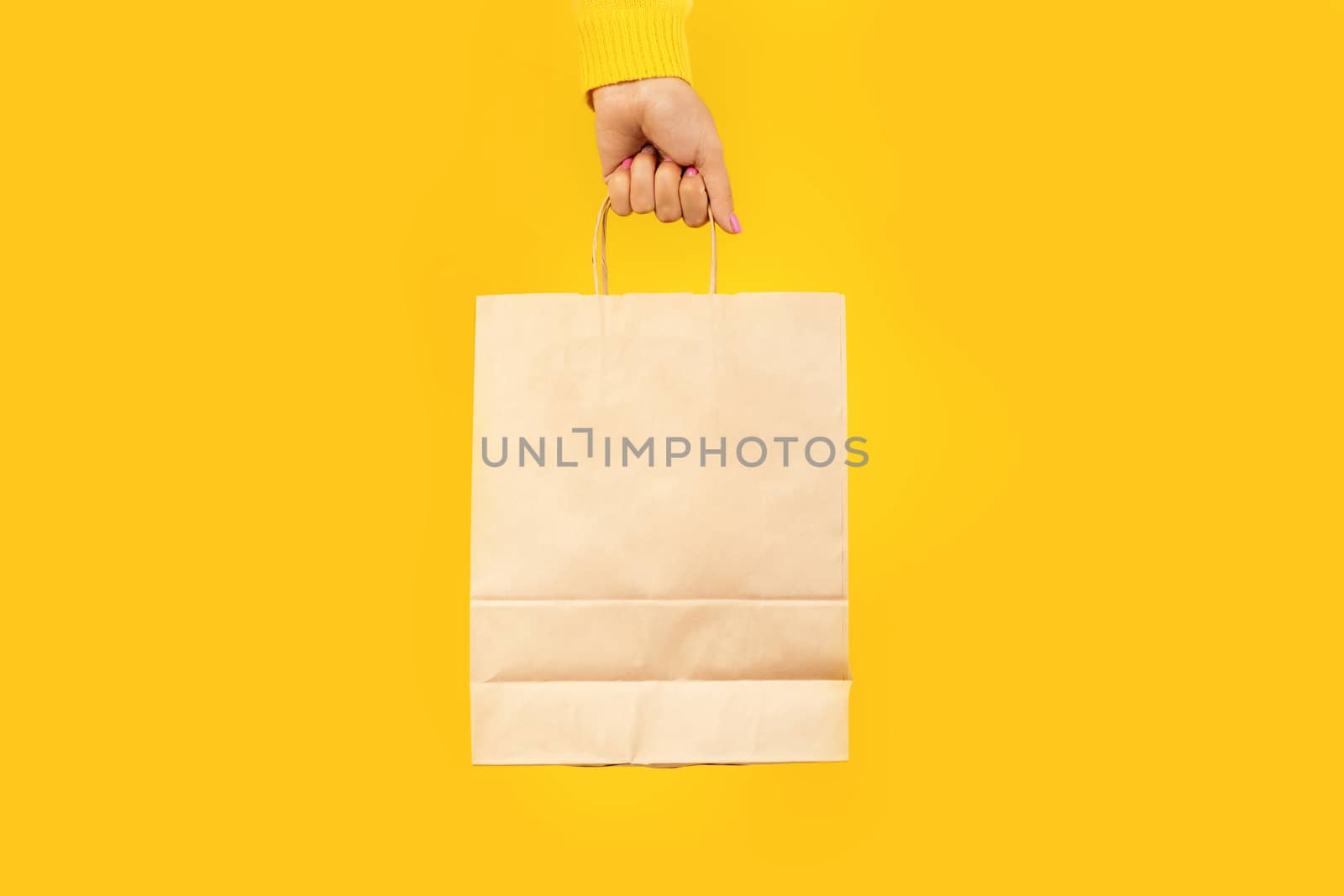 Woman hand holding paper shopping bag on yellow background. Shopping concept.