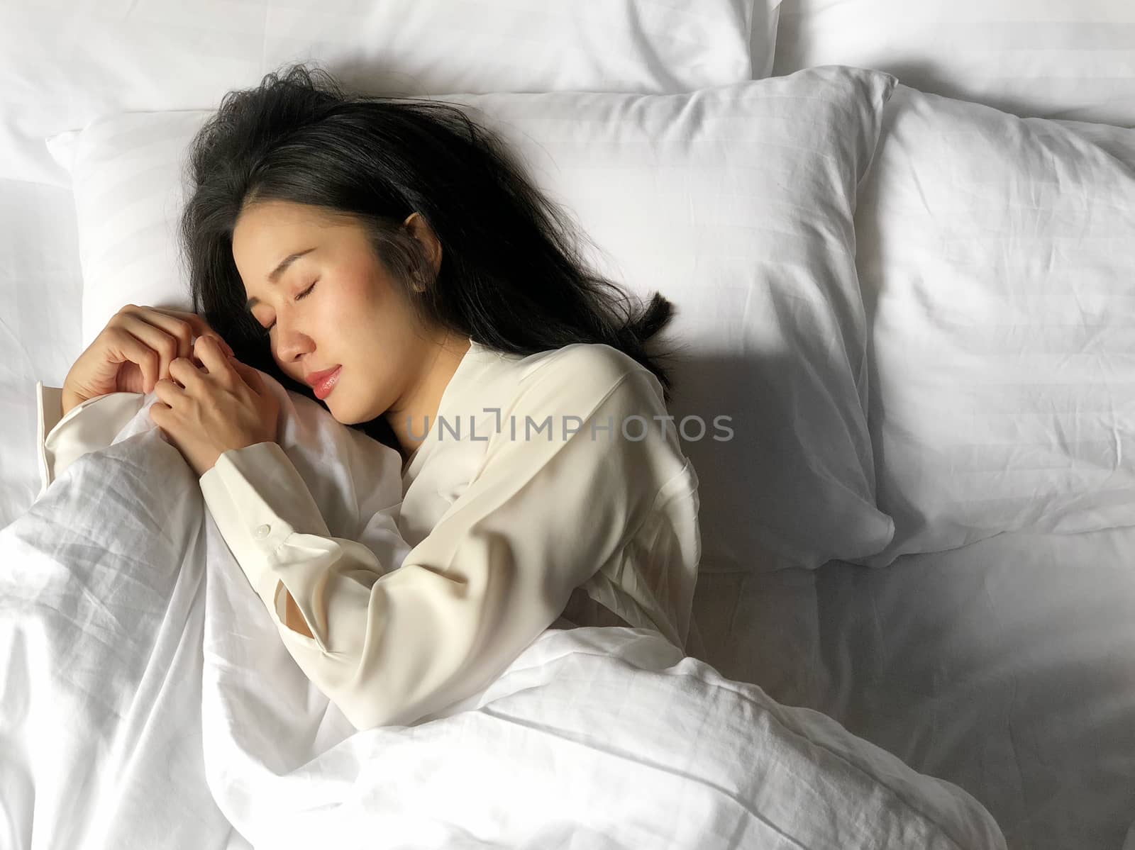 Beautiful asian woman sleeping in bed under white quilt with hea by Surasak