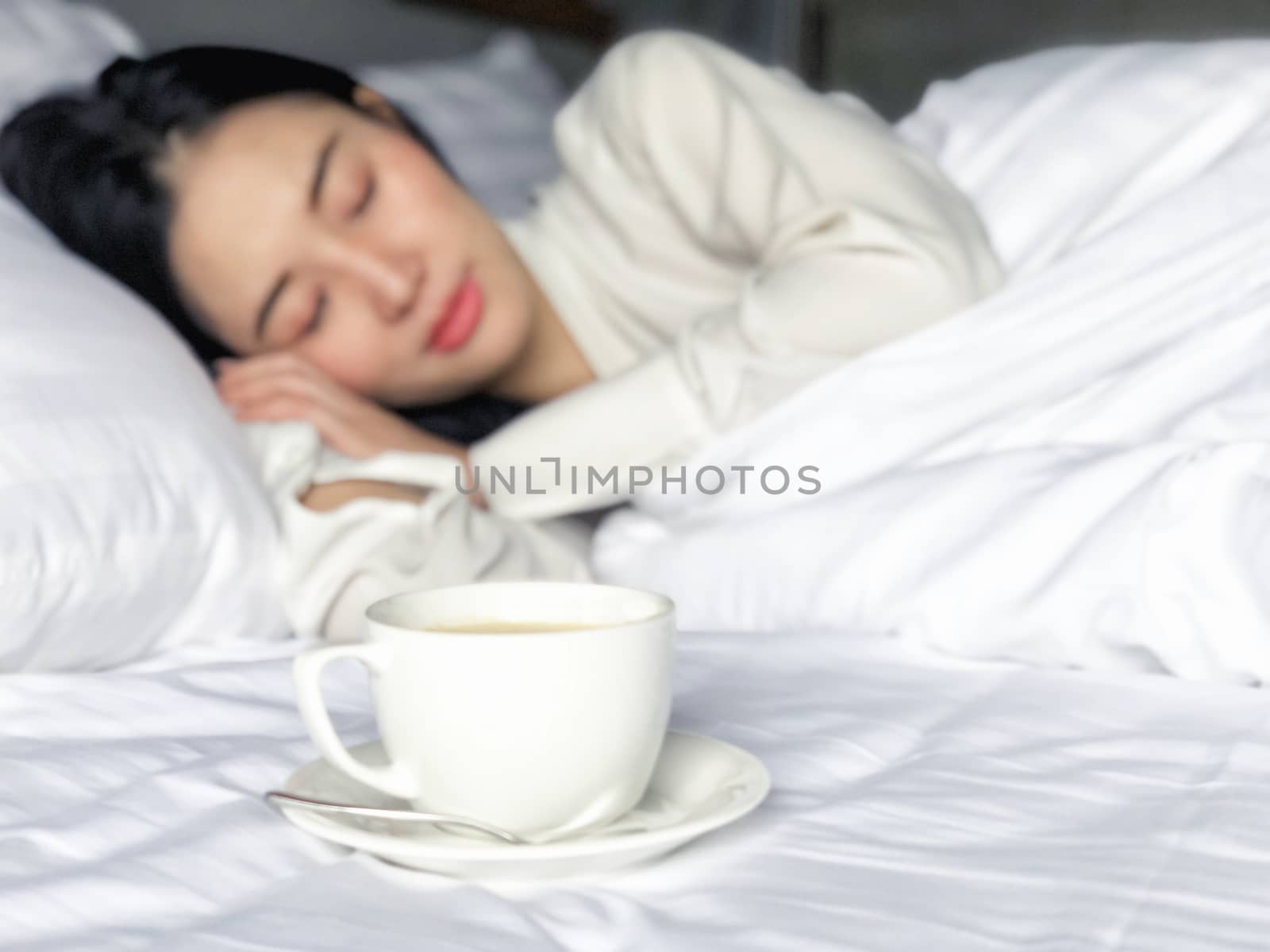 Beautiful Asian woman sleeping with a morning cup of coffee in b by Surasak