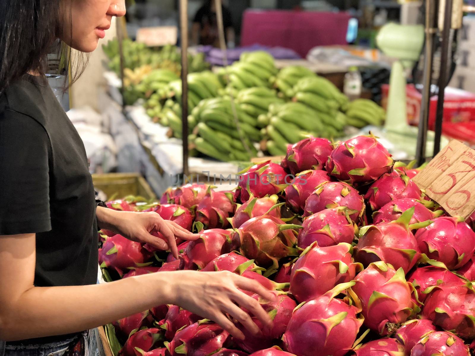 Woman choosing dragon fruits at a fresh market by Surasak