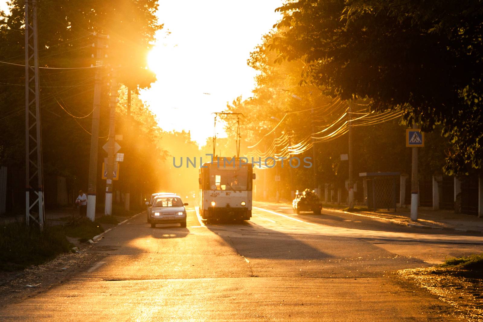 TULA, RUSSIA - JUNE 6, 2013: Car and tram on traffic light stop under golden sun backlight, Dust in the air volumetric glowing bright.