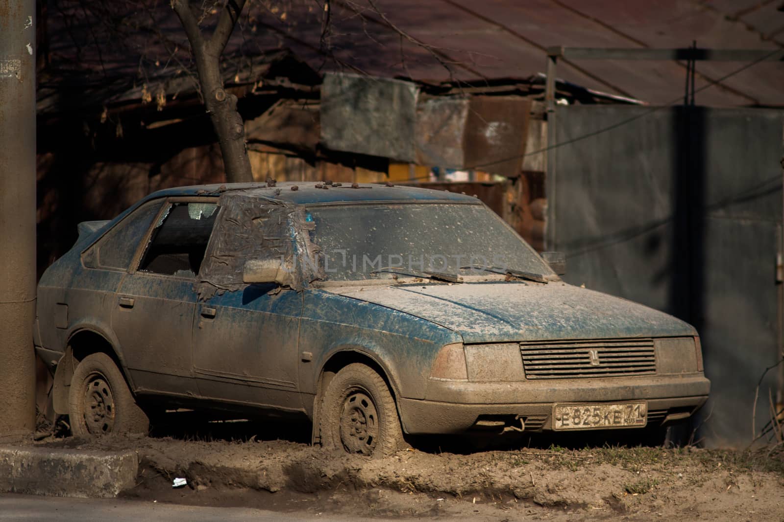 TULA, RUSSIA - APRIL 13, 2012: abandoned dirty car on side of spring road with slum ghetto background. Thick layer of dust over car.