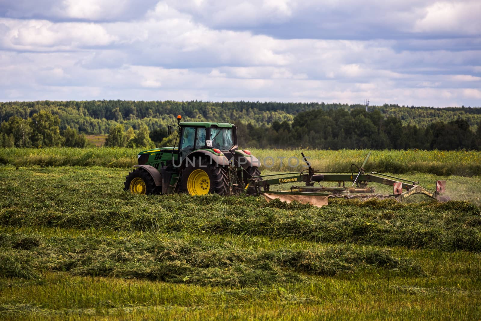 TULA, RUSSIA - JULY 30, 2019: green haymaking tractor on summer field before storm - telephoto shot with selective focus and blur.
