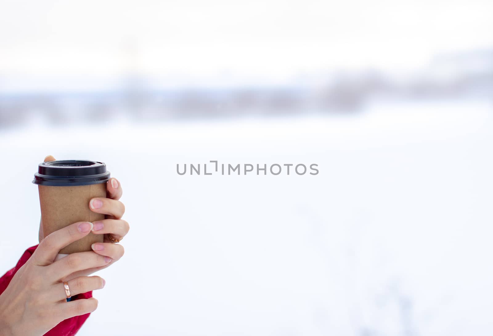 A young woman in a red jacket in winter holds a glass of hot coffee or tea. A snowy winter and a hot drink to keep you warm.