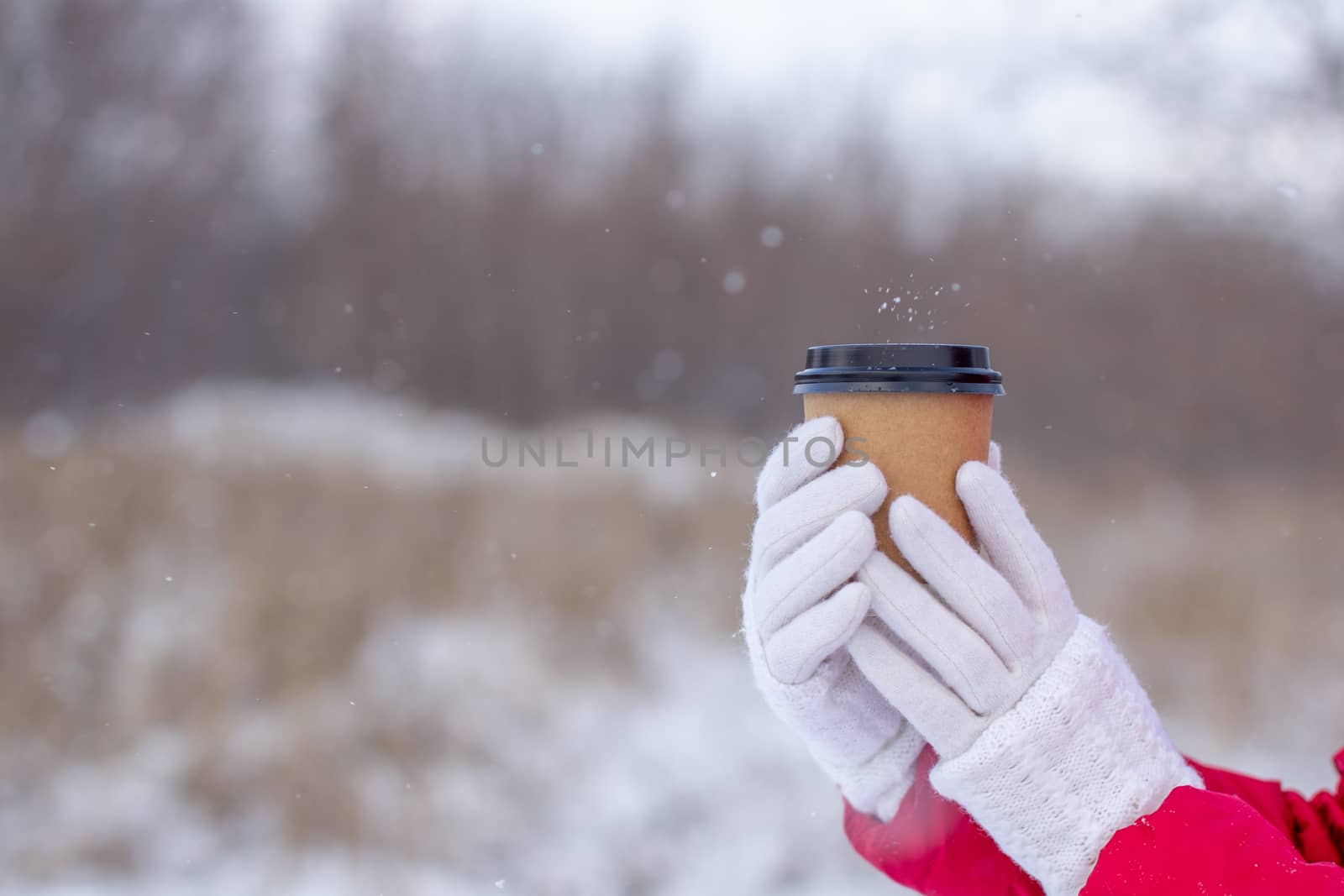 A young woman in a red jacket in winter holds a glass of hot coffee or tea. A snowy winter and a hot drink to keep you warm.