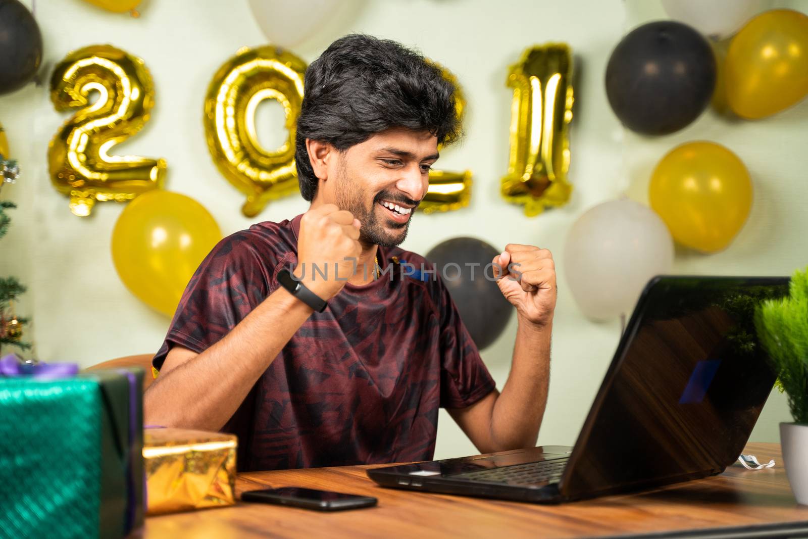 Concept of good news, job offer or luck during 2021 new year showing by happy excited young man in front of laptop with new year decorated background at home