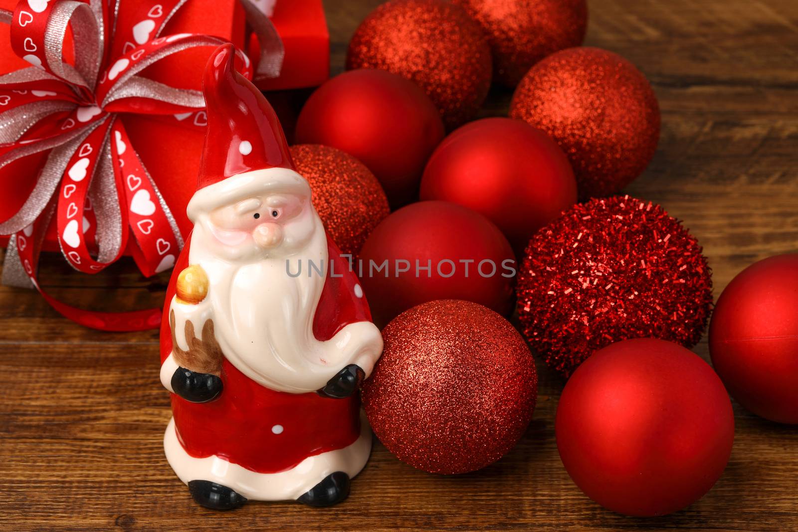 A ceramic Santa with red Christmas baubles and present boxes on wooden background.