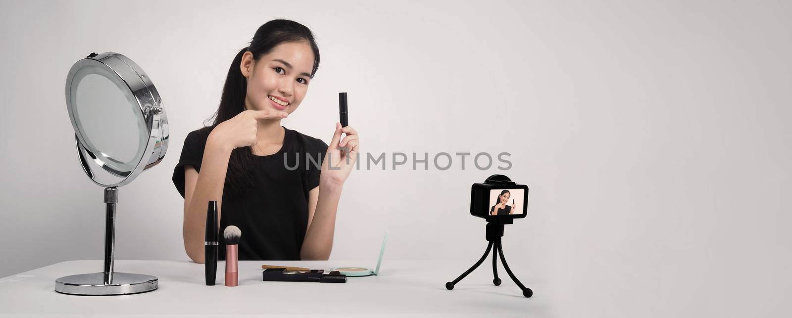 Asian teen woman sit in front of camera and live broadcasting as a beauty blogger influencer or youtuber to review or advice about how to make up at home. studio shot white background.