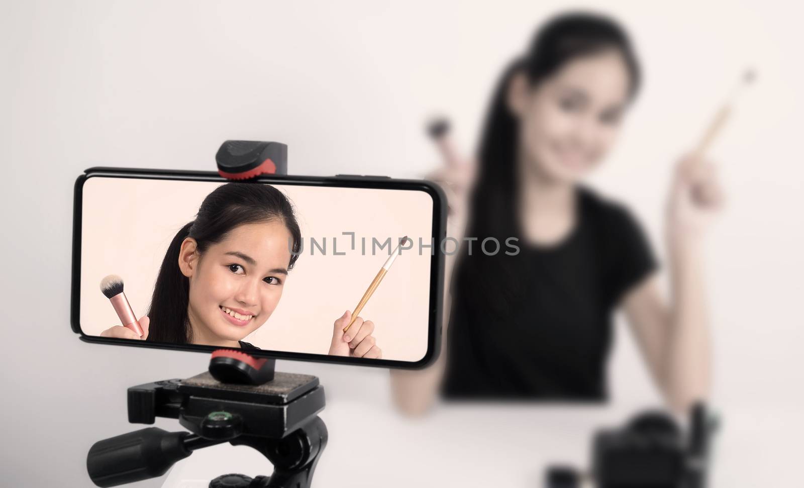 Asian teen woman sit in front of camera and live broadcasting as a beauty blogger influencer or youtuber to review or advice about how to make up at home. studio shot white background.