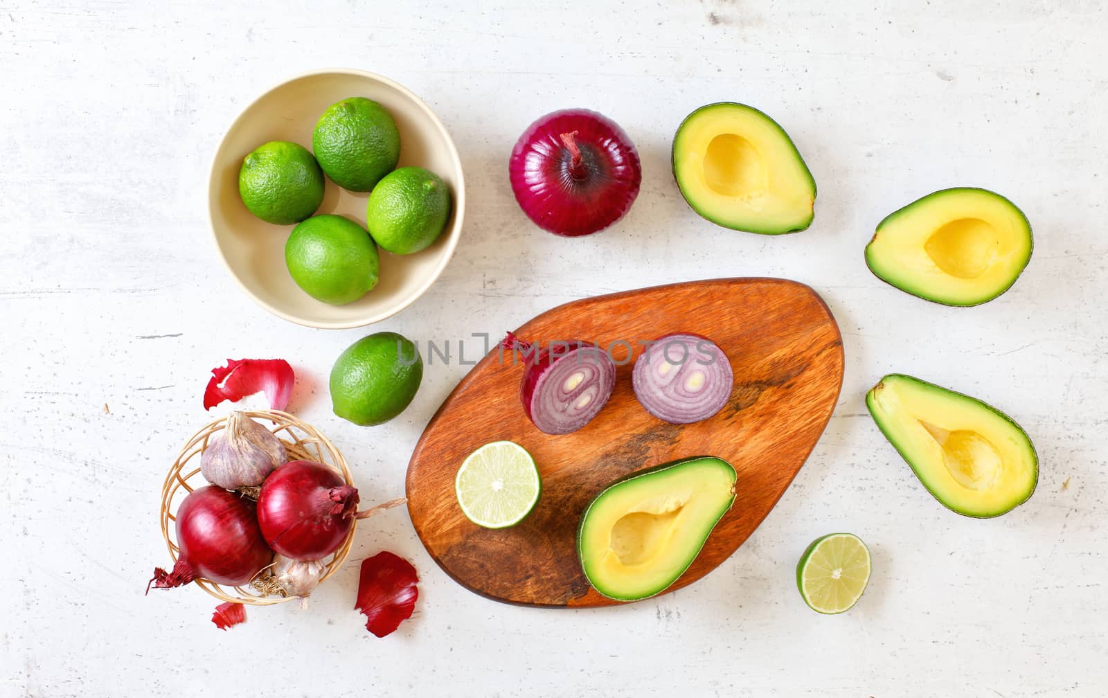 Avocado halves, limes and onions - basic guacamole ingredients on white working board, flat lay photo.