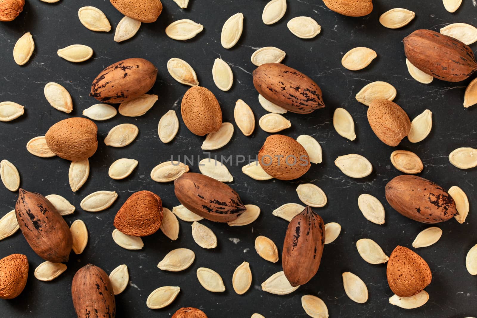 Whole almonds, pecan nuts and pumpkin seeds mixed on black marble like board, view from above.