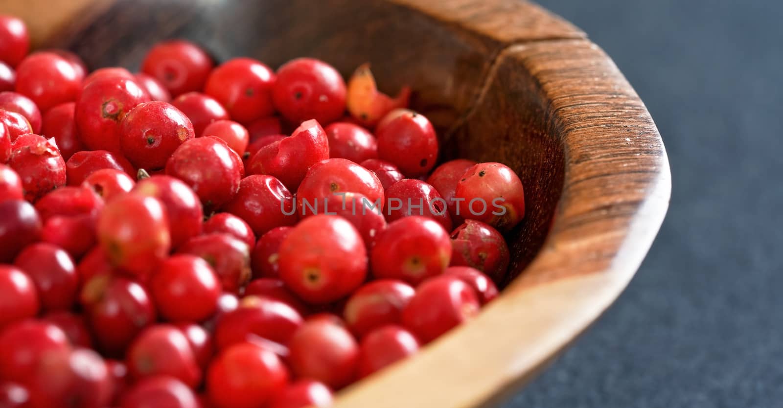 Whole pink red peppercorns in small wooden bowl, closeup detail by Ivanko