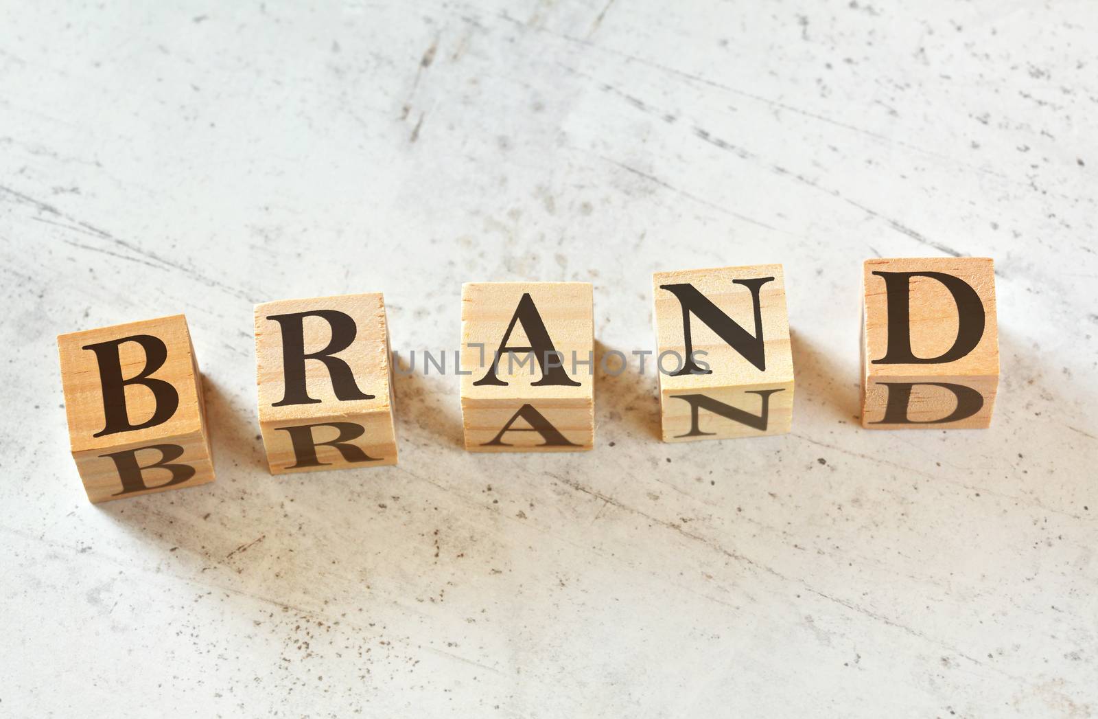 Five wooden cubes with word BRAND on white stone like board, view from above.