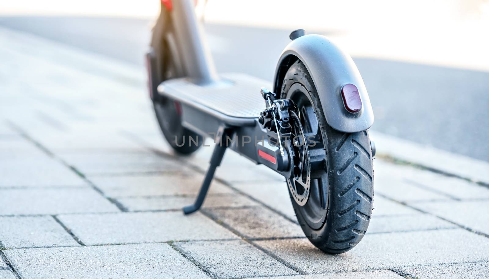 Electric scooter parked on tiled stone pavement - closeup detail on rear wheel.