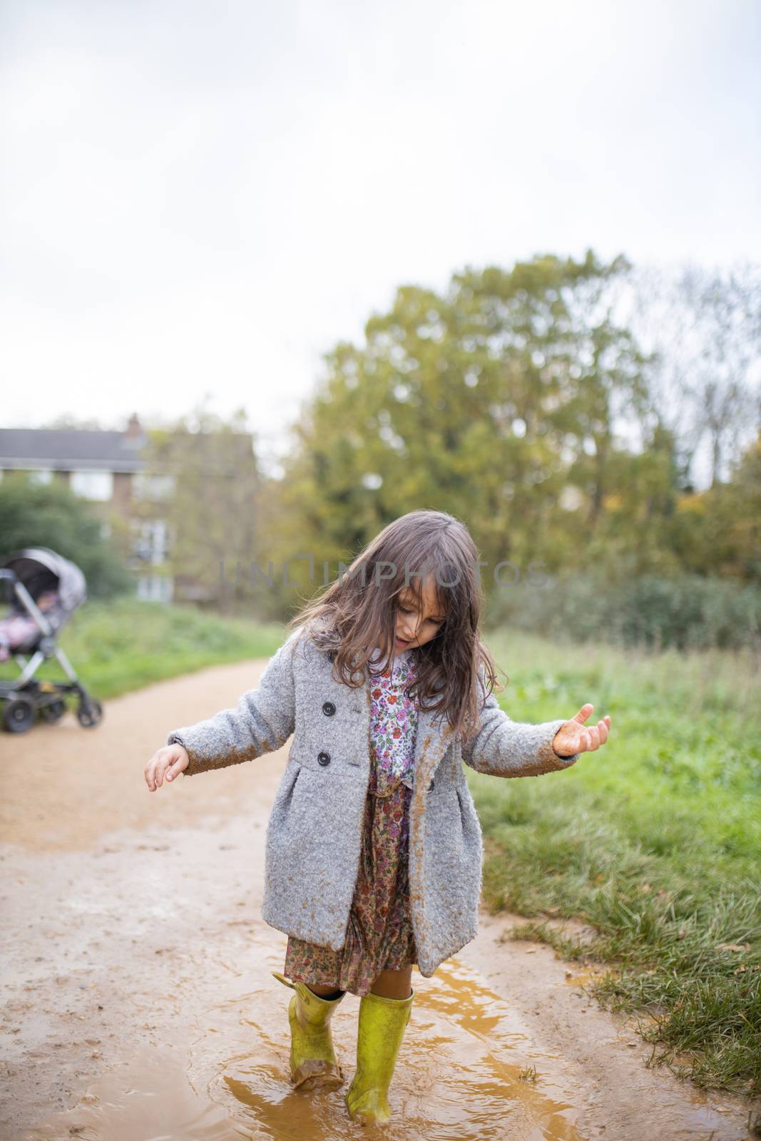 Happy little girl calmly walking through a muddy puddle by Kanelbulle