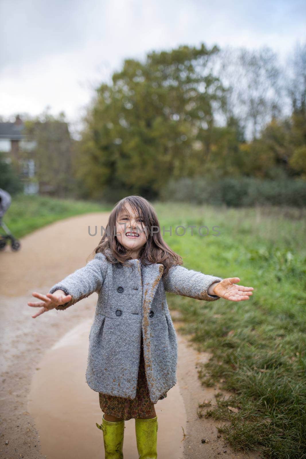 Happy and adorable little girl smiling after jumping in a muddy puddle. Young child having fun and getting dirty in puddles. Kids playing outside
