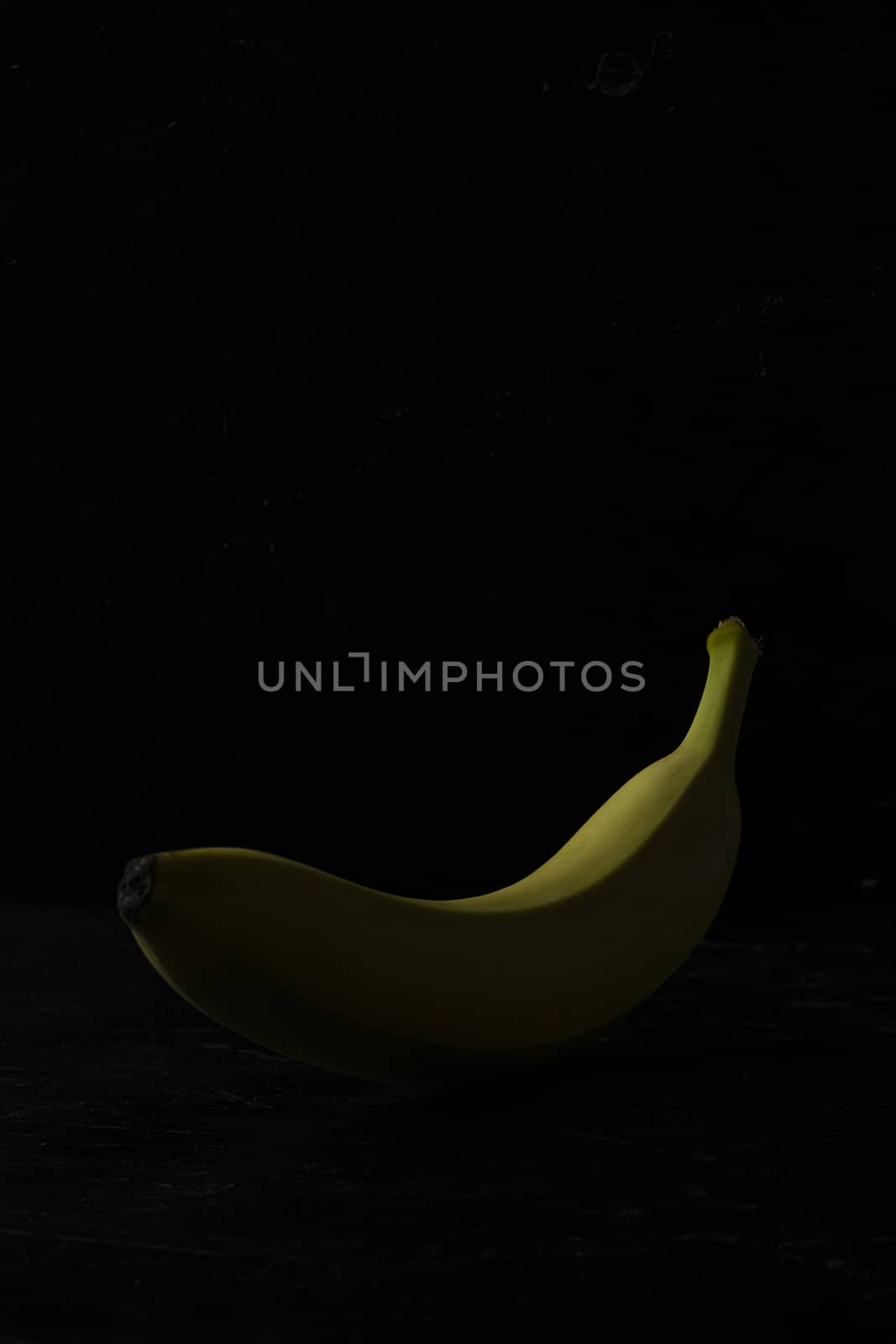 Single yellow banana on black wooden background by sashokddt