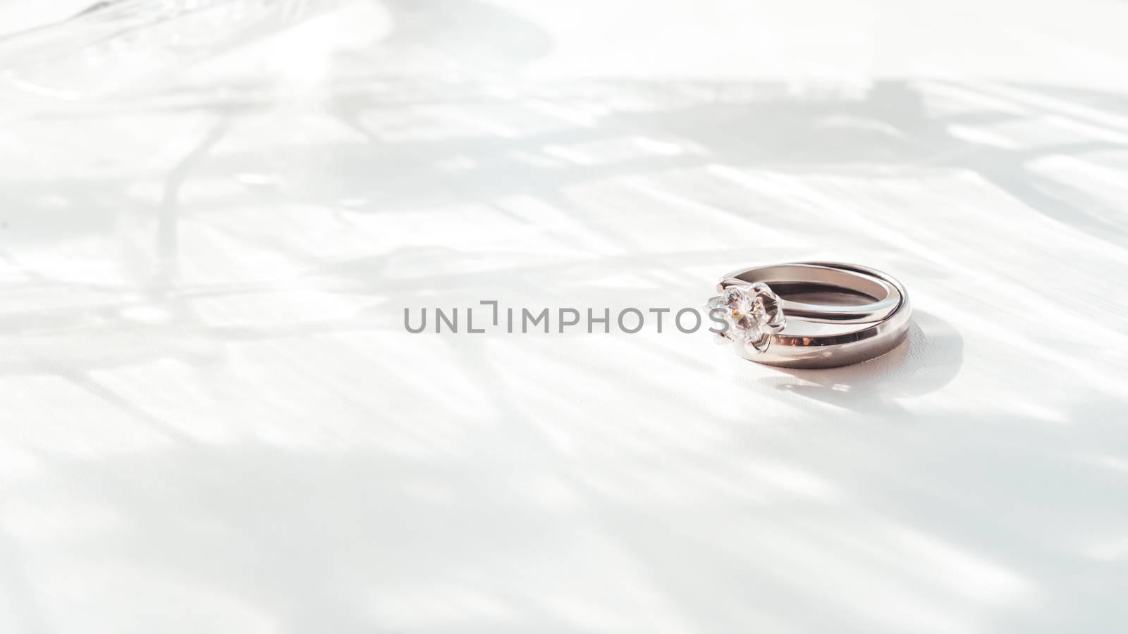 Wedding and engagement rings with diamond. Symbol of love and marriage on white background with laced shadow. Sunlight on white background.