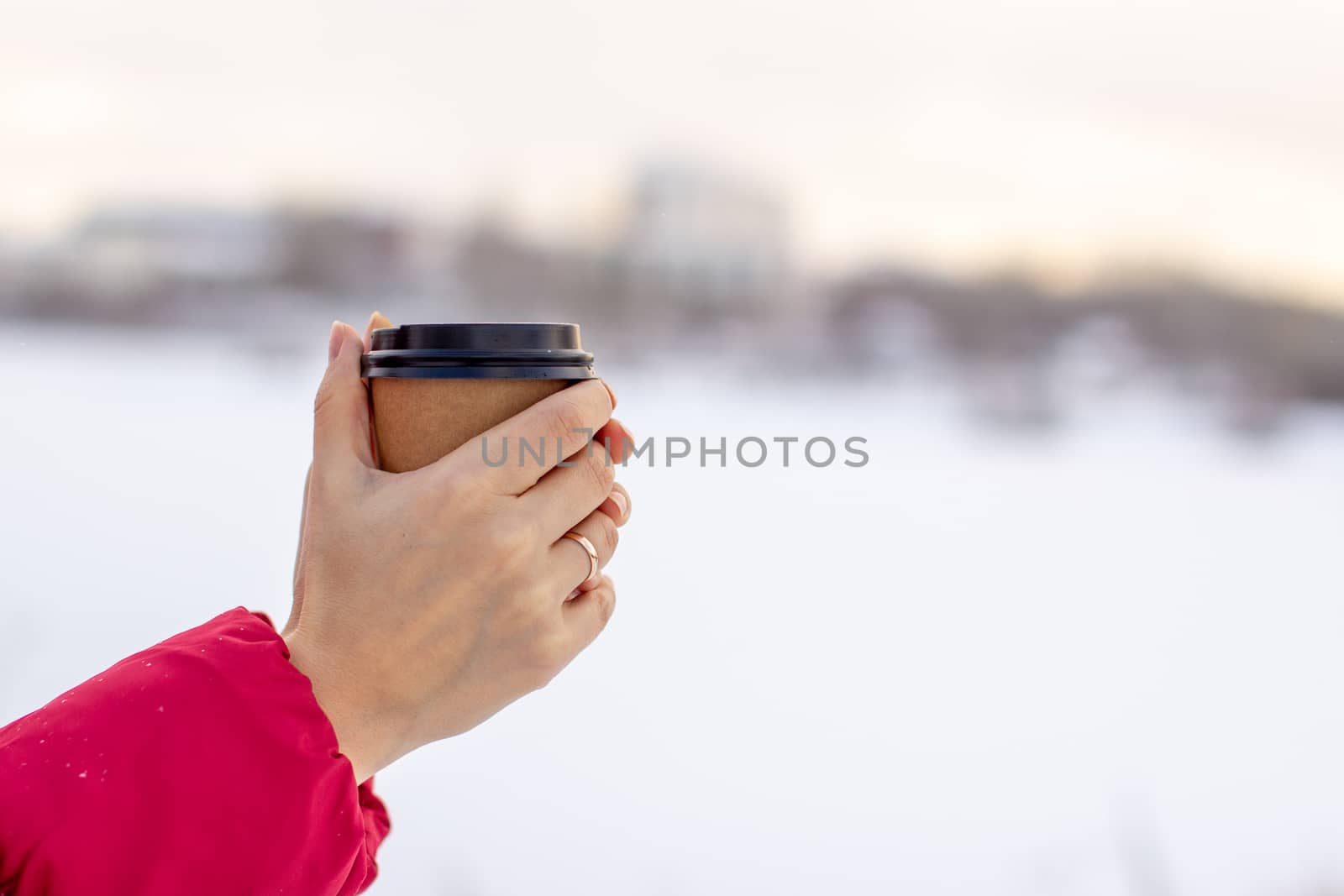 A young woman in a red jacket in winter holds a glass of hot coffee or tea. A snowy winter and a hot drink to keep you warm. A glass of coffee in winter.