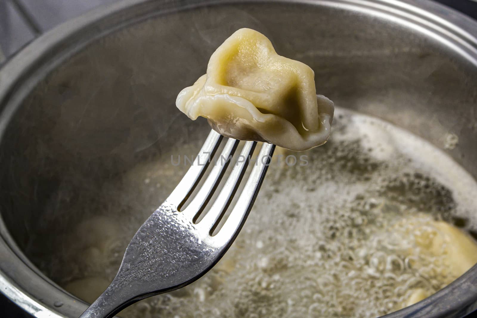 dumplings are put on a fork against the background of boiling broth by Akmenra