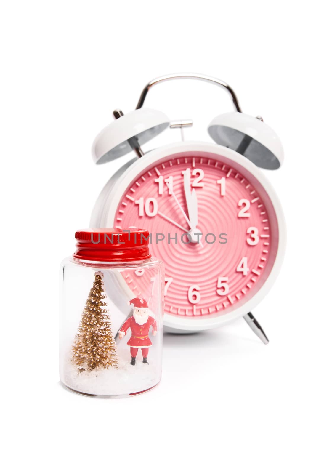 Festive alarm clock showing a minute before midnight next to a Christmas ornament with Santa Clause and a Christmas tree with snow, isolated on white background. Christmas and New Year concept.