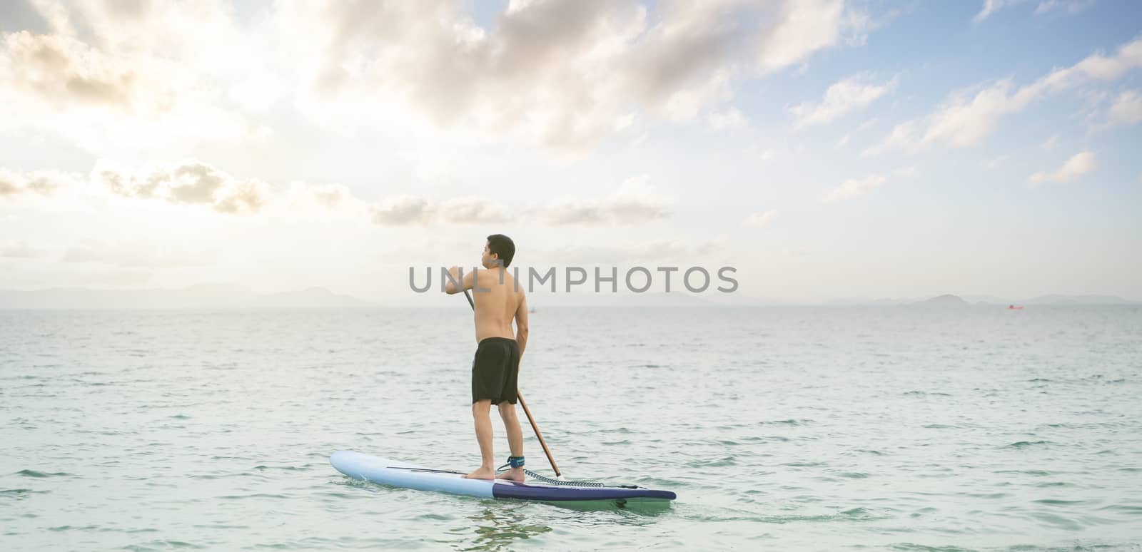 Asian man is paddling on a SUP board, standup paddler at the oce by sirawit99