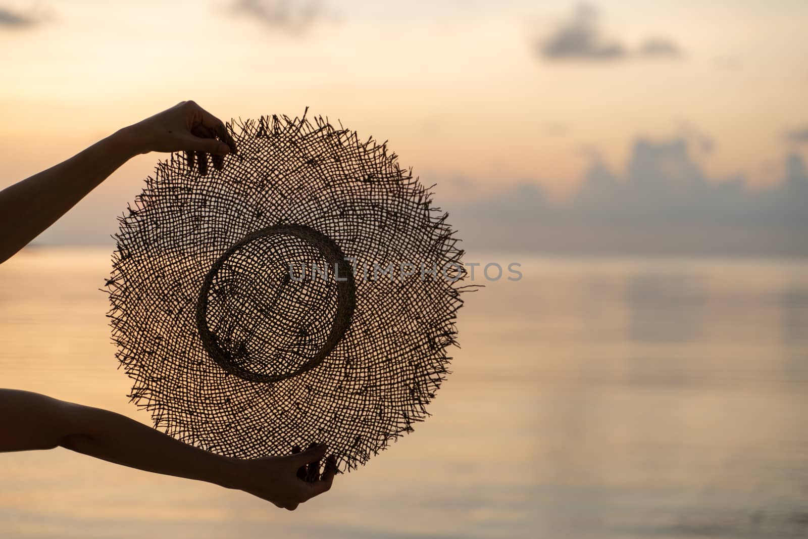 Female hands hold summer straw hat with sunset view. Vacation concept