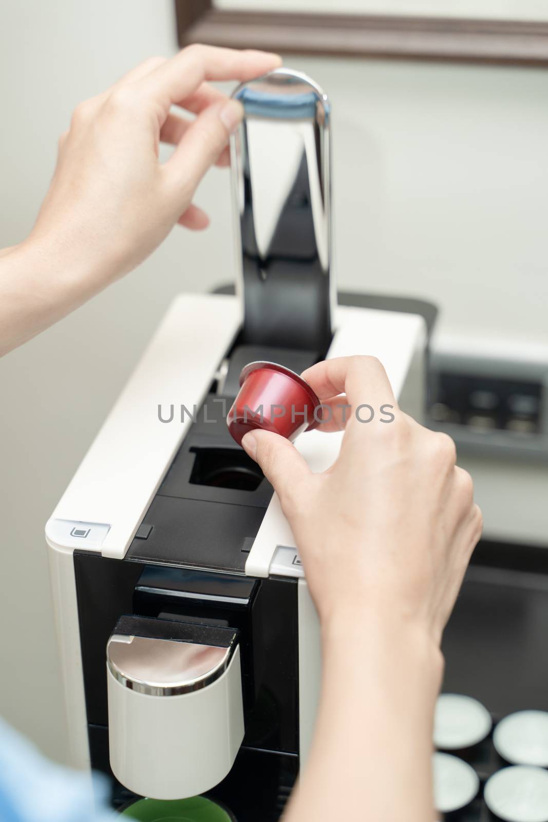 Close up of woman hand pressing button on a capsule into a coffee machine.