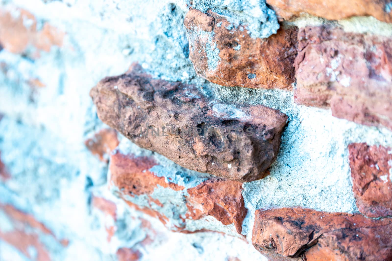 A brick wall with white mortar, photographed at a slight angle, in which the bricks stand out of the wall unevenly and are partially broken.