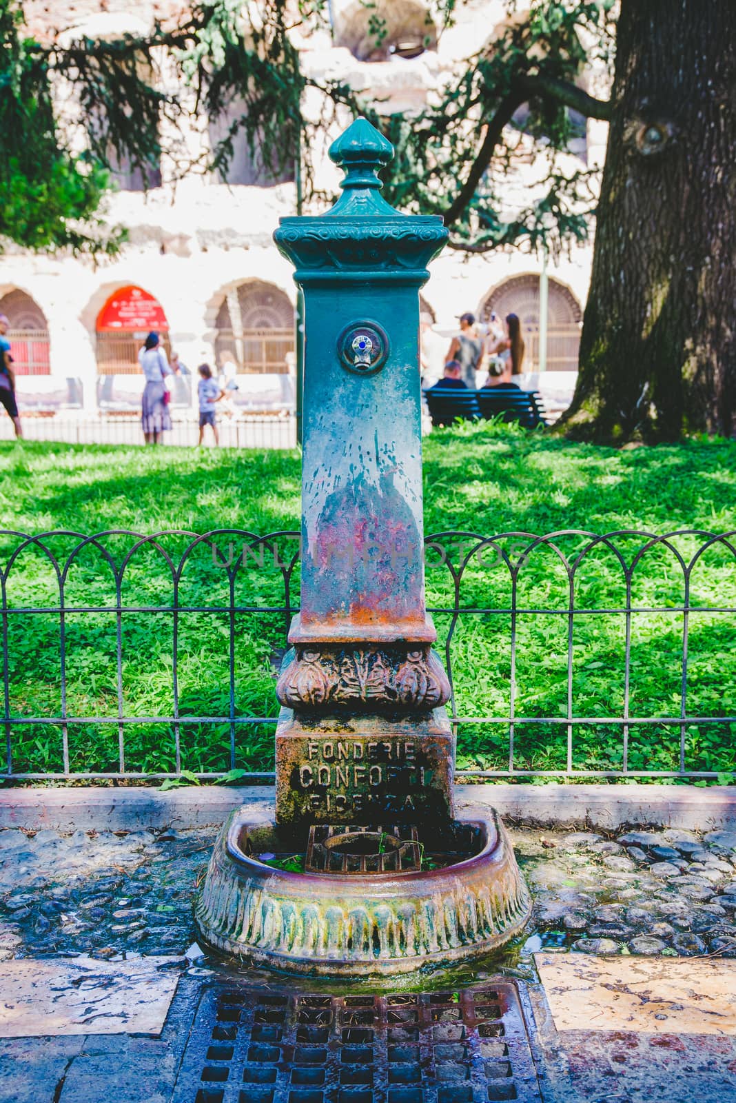 An old, nostalgic and antique drinking fountain in Verona, Italy. It is made of metal and already shows many traces of rust on the fountain and drain, but has a modern tap.