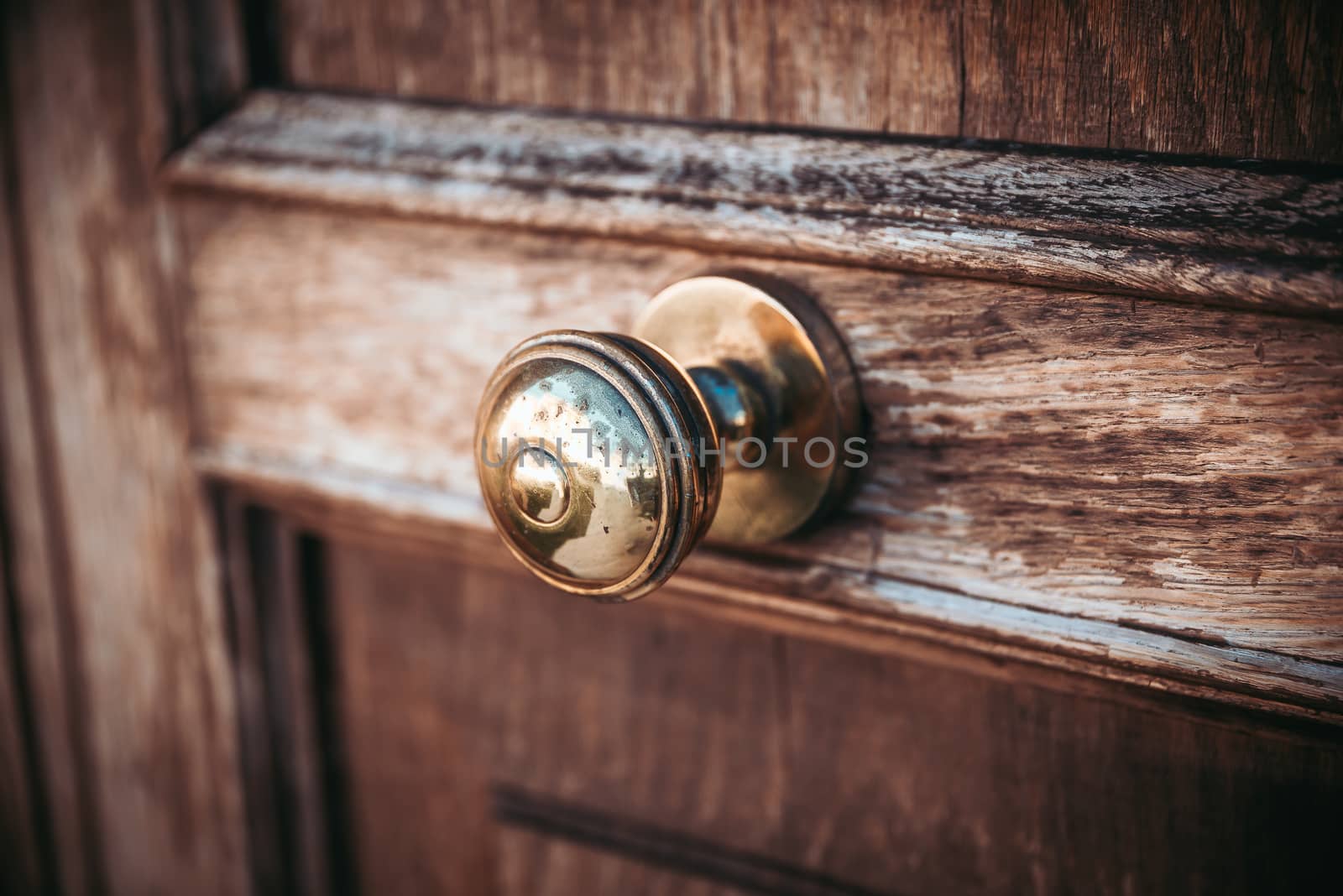 An old, nostalgic metal doorknob on a dark wooden door, the surface of which is already slightly corroded and worn and is attached to the middle of the door.