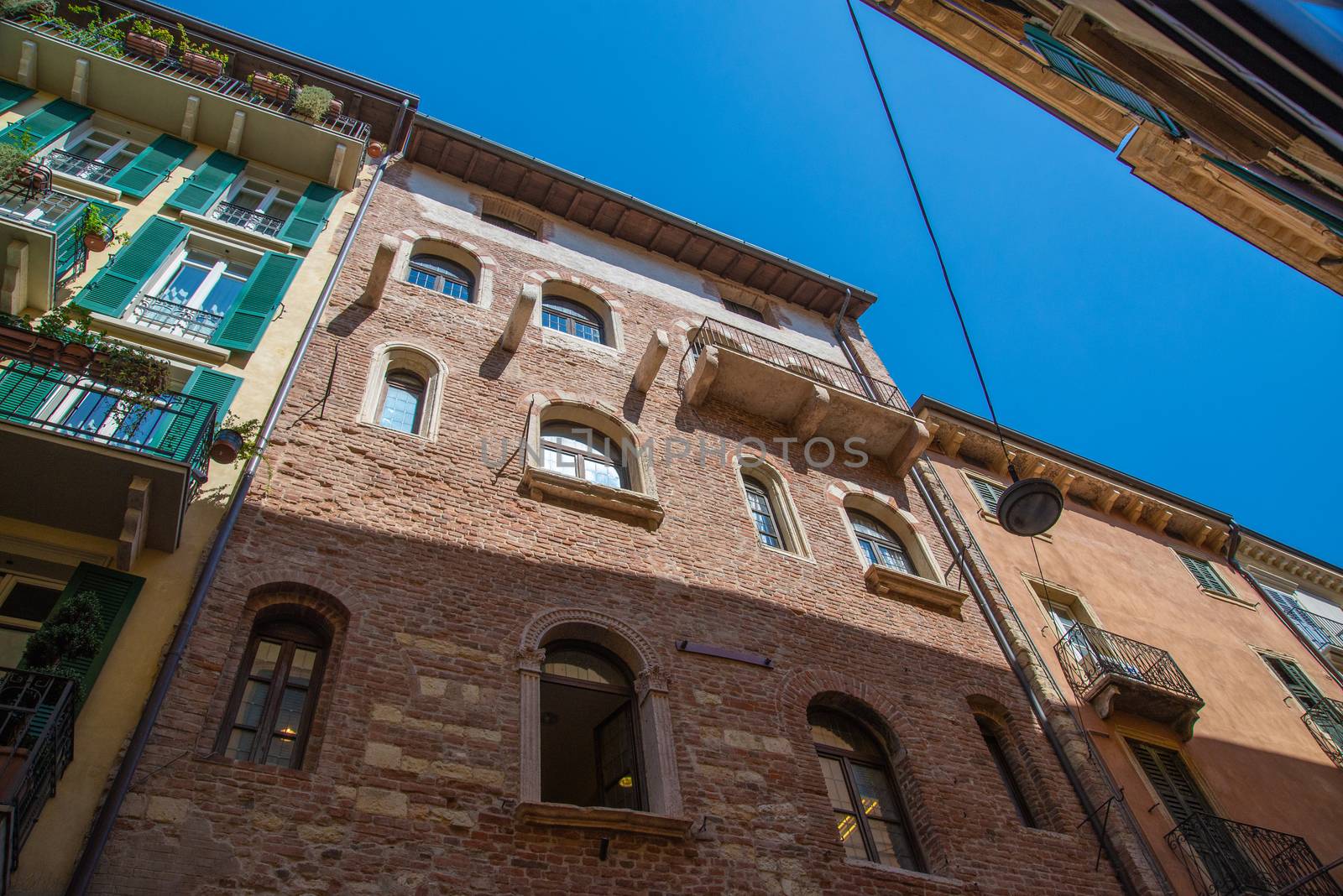 Verona, Veneto/Italy - 18.08.2020: View from a narrow alley of a historic house front up to the sky with antique restored houses made of brick, metal and wood