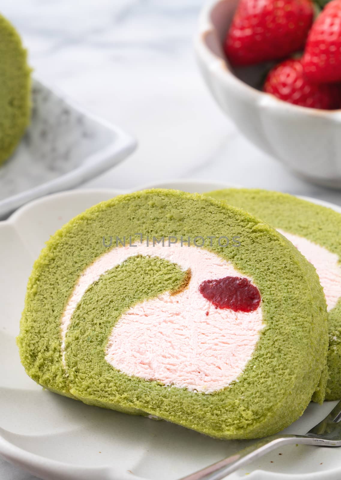 Delicious Matcha Swiss Roll Cake slices with strawberry icing cream on white background, close up.