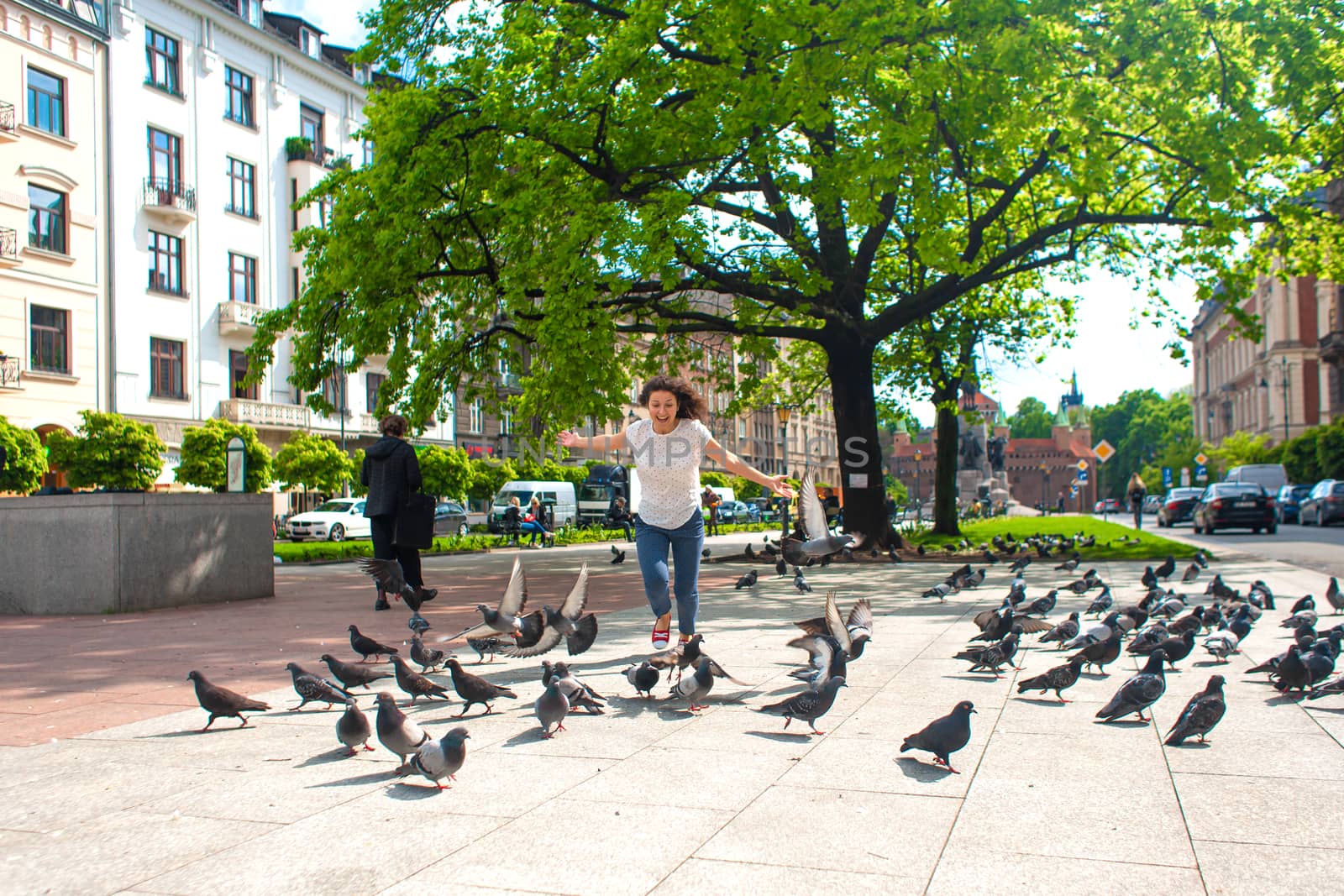A girl scares a flock of pigeons in the city square.