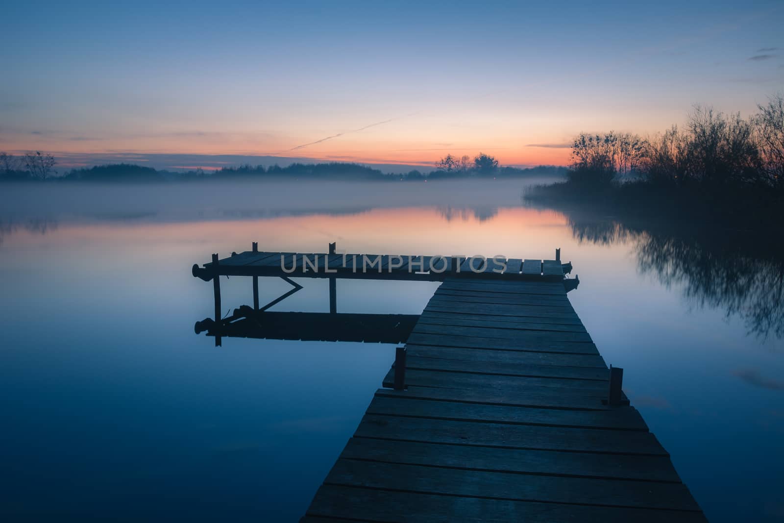 Wooden platform on a calm blue lake after sunset, evening landscape