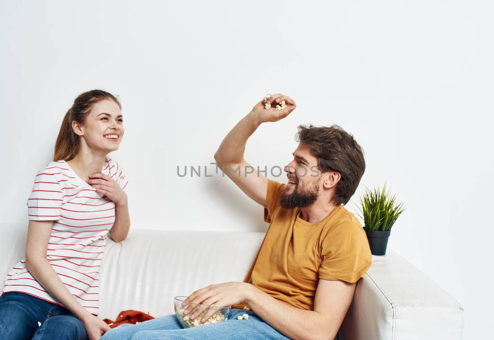 A man and a woman on a white sofa In a bright room a plate of popcorn and friends a flower in a pot. High quality photo