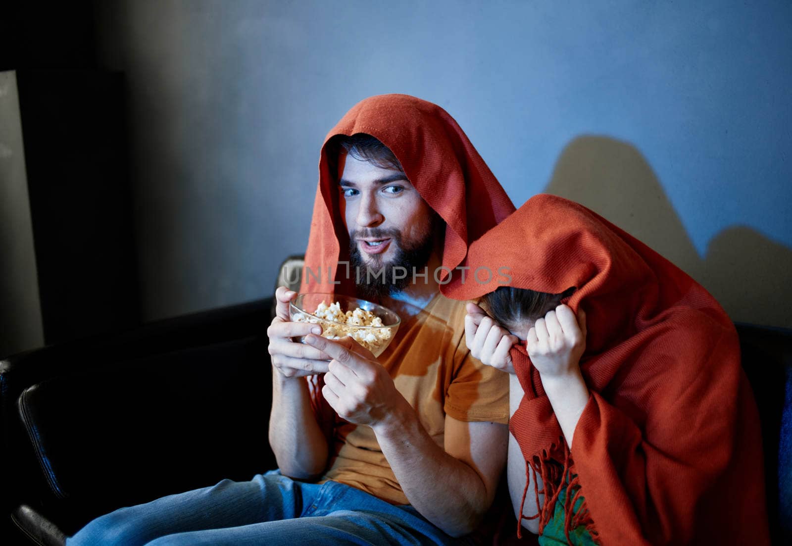 scared woman with a red plaid on her head and a man with a plate of popcorn in a dark room. High quality photo