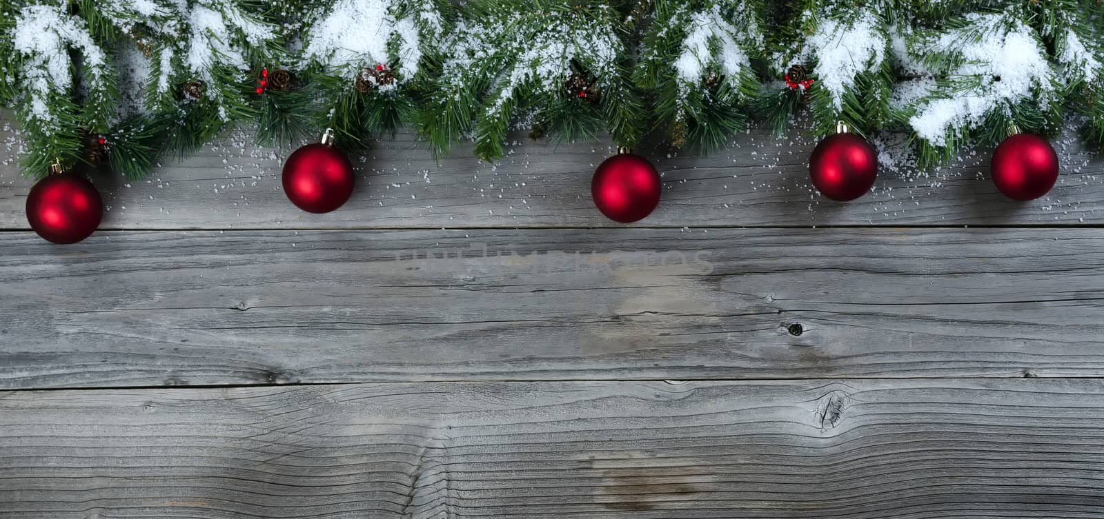 Christmas rustic natural wooden background with snow covered evergreen branches and red ball ornaments   