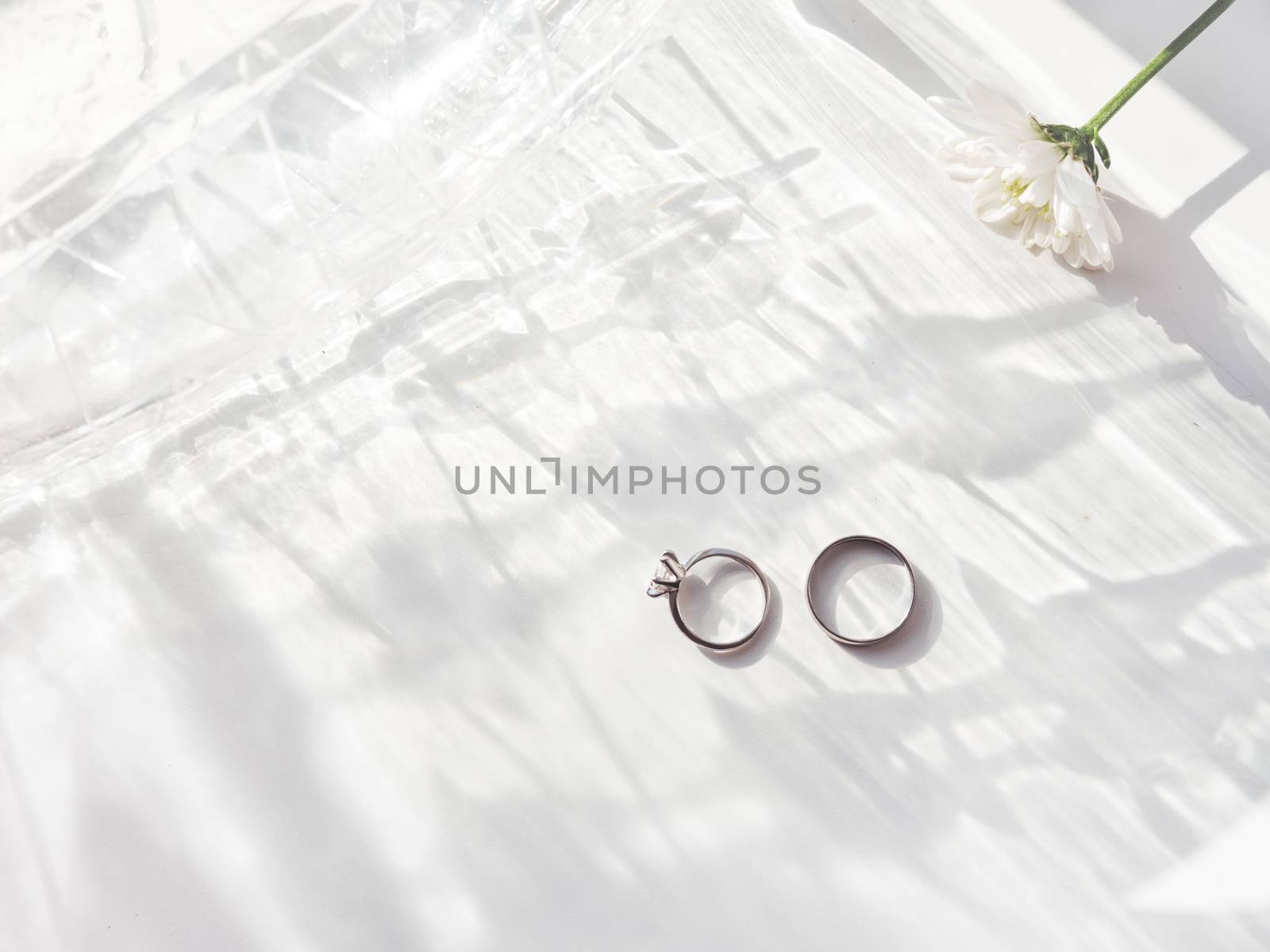 Top view on wedding and engagement rings with diamond. Symbol of love and marriage on white background with laced shadow. Sunlight on white background.