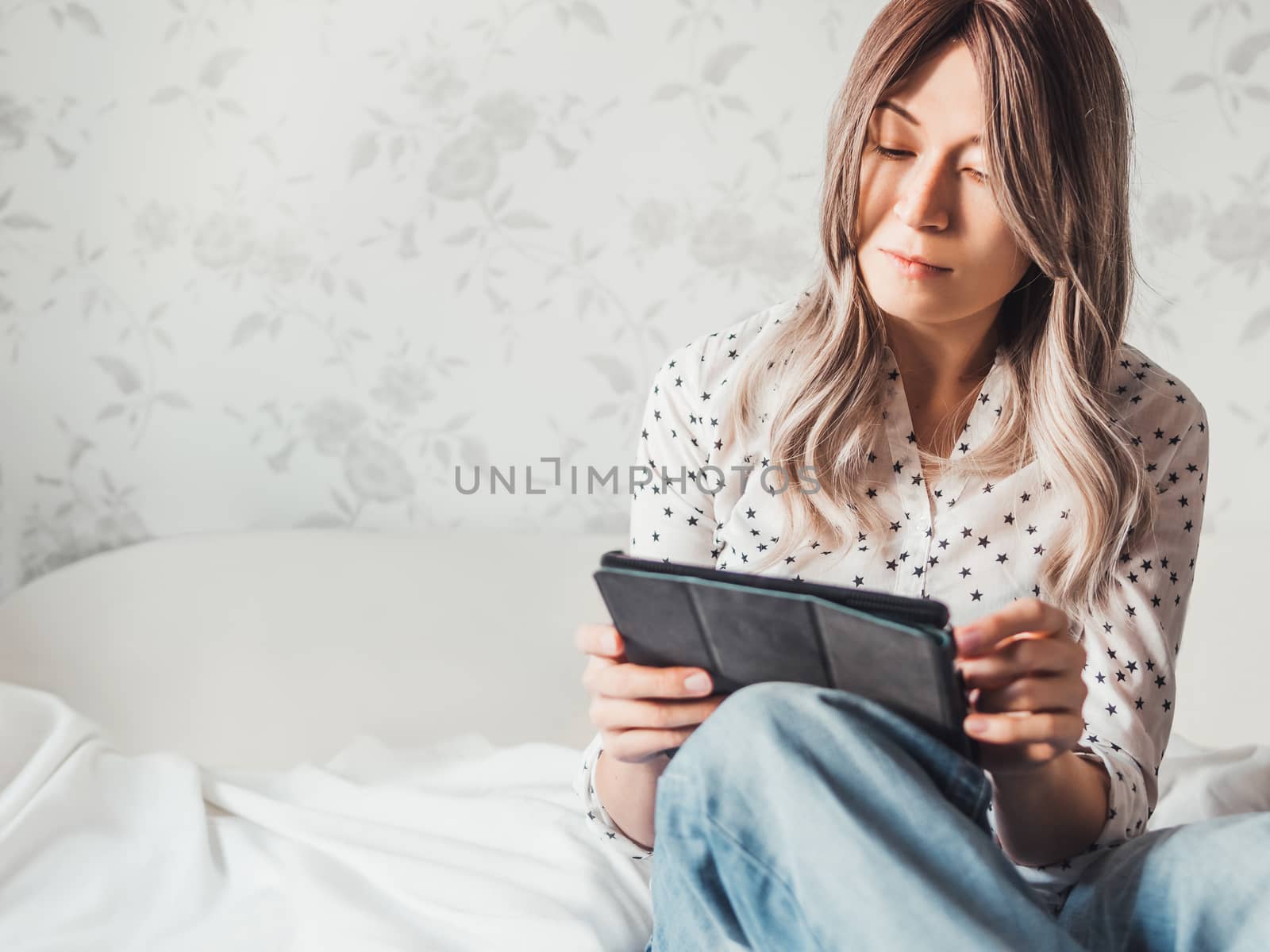 Woman sits on bed with tablet PC. She watches online TV series. Online video call or conference, distance learning, remote education. Self isolation during quarantine.