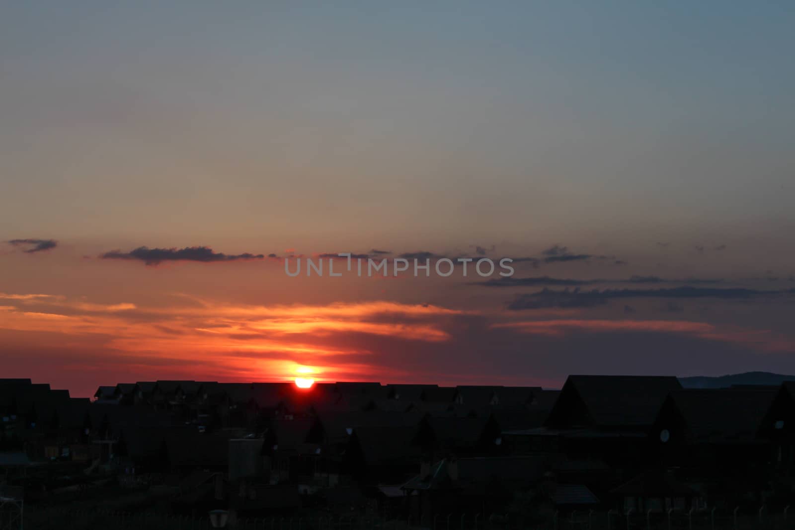 Sunset behind the houses with orange sky and clouds by codrinn