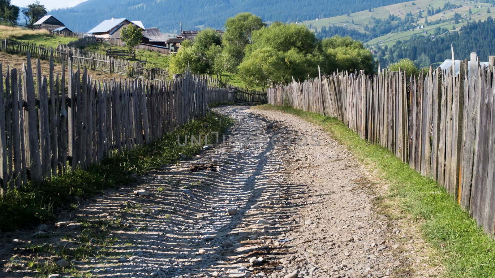 Road with ballast in the mountains with houses - fence in the mountains