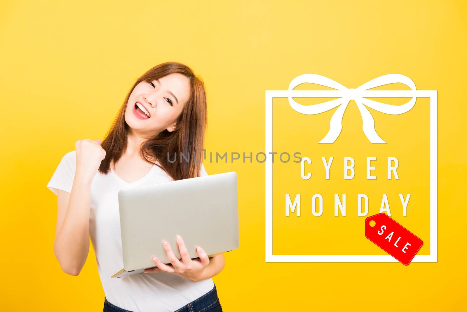 Asian happy portrait beautiful cute young woman teen smile standing hold laptop computer and excited celebrating success with Cyber Monday in the gift box on space, studio shot yellow background