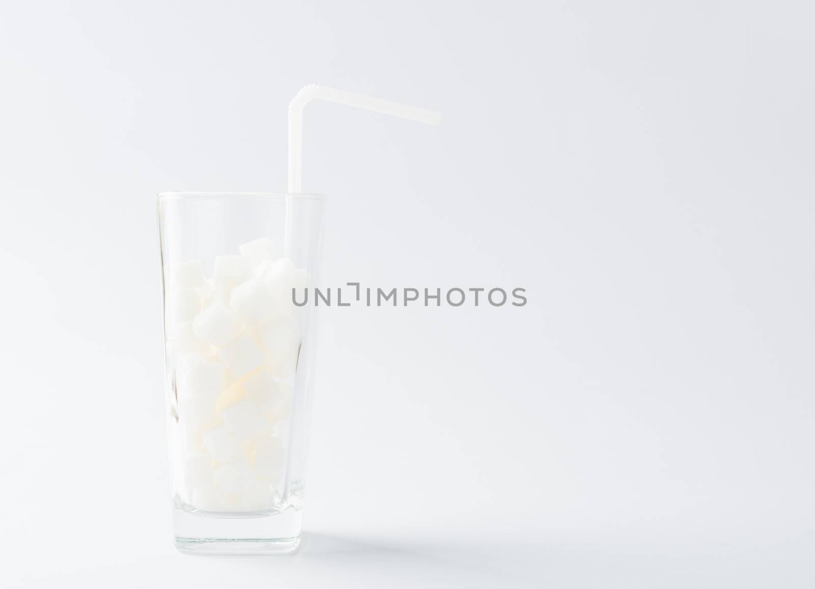 A glass full of white sugar cube sweet food ingredient, studio shot isolated on white background, health high blood risk of diabetes and calorie intake concept and unhealthy drink