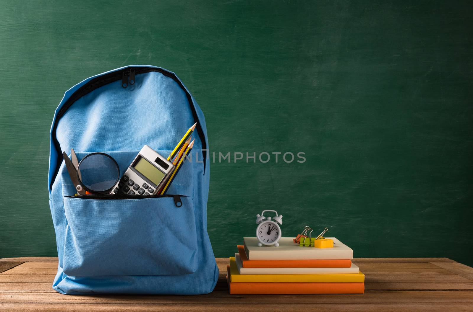 Front of stylish school bag backpack and stationery accessory on a table desk at the green chalkboard, Back to school education concept