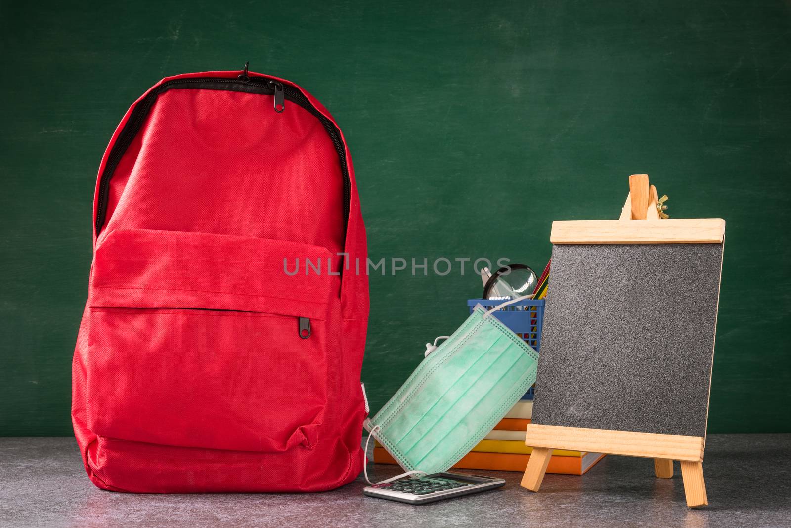 Front school backpack and accessories with face mask protect on table at chalkboard, student bag supplies at classroom backboard, Back to school education new normal outbreak COVID-19 or coronavirus