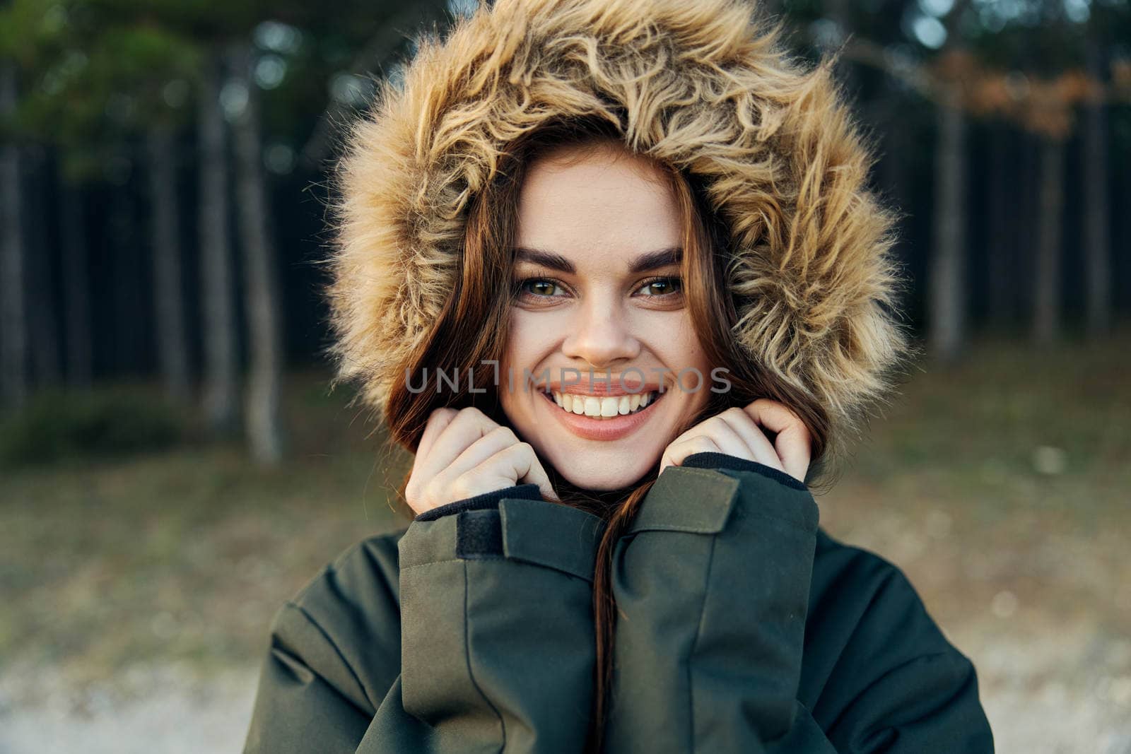 Smiling woman with a hood on her head in a warm jacket close-up nature on a forest background. High quality photo