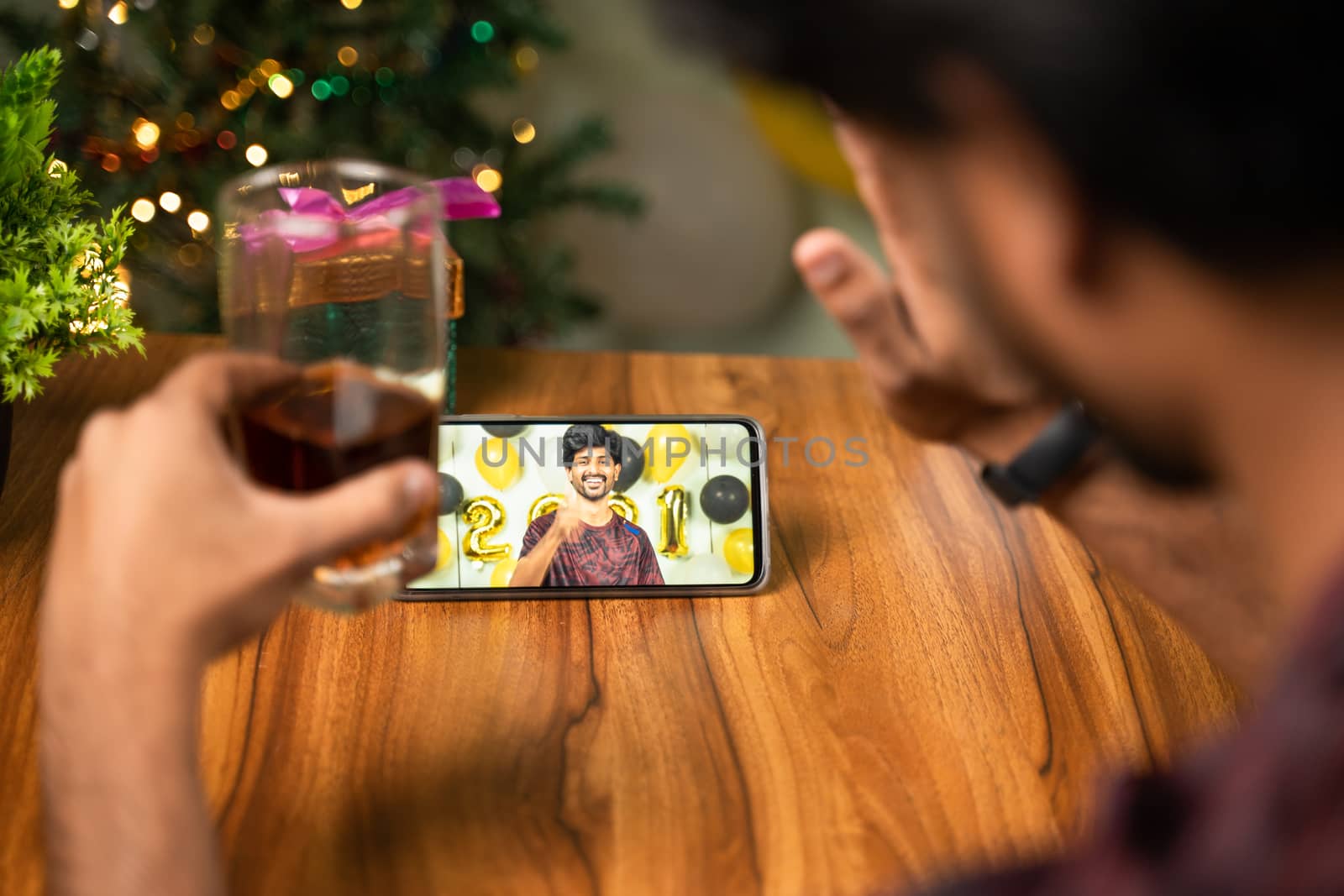 Shoulder shot of young man partying during new year or Christmas celebration video call on mobile - concept of distance holyday celebration due to coronavirus or covid-19 pandemic. by lakshmiprasad.maski@gmai.com